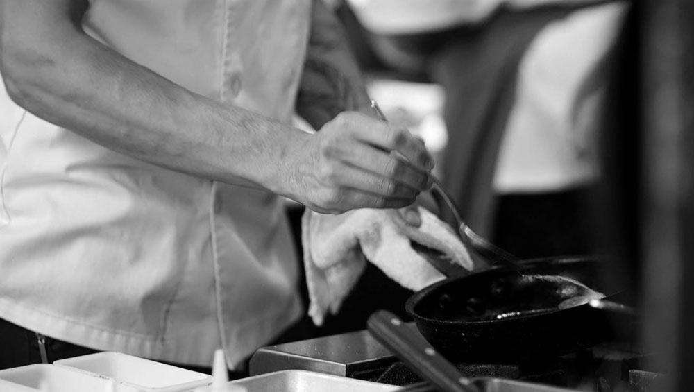 close-up of chef's hand basting pork chop in an iron skillet with a metal spoon